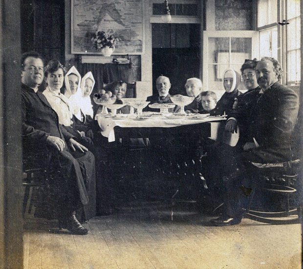 Photo noir et blanc. Ce sont 11 membres de la famille LePailleur assis à la table. On retrouve Georges-Marie, Soeur Agnès, Alfred-Narcisse, Philomène, Célina-Elmire et Joseph-Adélard.