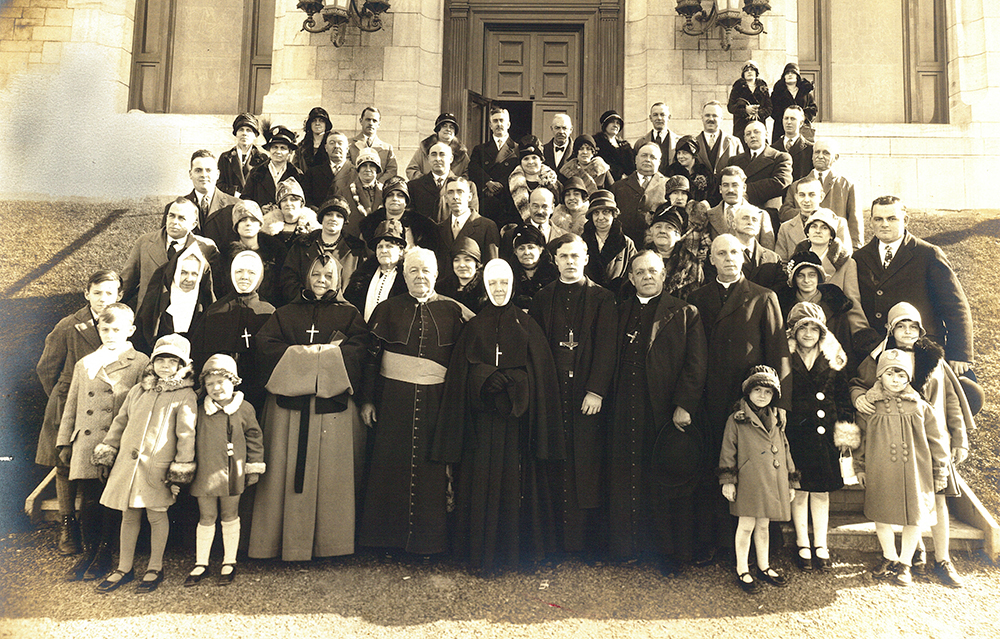 Photo noir et blanc d'un groupe d'une cinquantaine de personnes devant une église. 8 religieux sont en avant-plan dont Monseigneur Georges-Marie et Soeur Agnès.