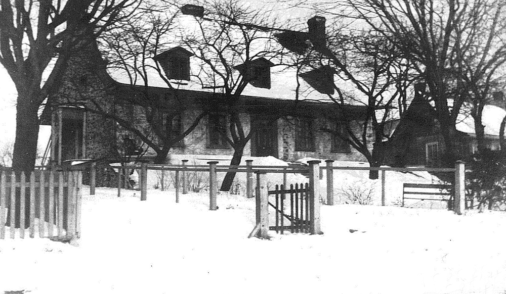 Photo noir et blanc de la Maison LePailleur en hiver, une grande maison québécoise en pierre au toit en pente à trois lucarnes.