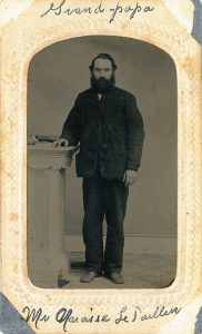 Tintype of young Alfred-Narcisse LePailleur. He is standing in a studio setting. His hand is on a column on which is a book.