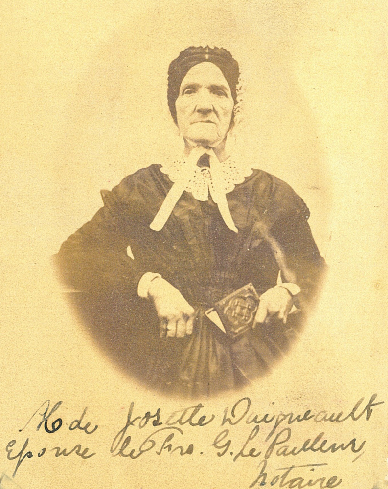 Photo noir et blanc de la veuve Josephte Daigneault (femme du notaire F-G LePailleur) en robe noire et bonnet blanc. Elle a un petit album dans sa main gauche.