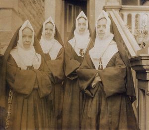 Black and white picture of Sister Sainte-Anne (Odile LePailleur) on the left, with her niece Hélène and two other members of the Notre-Dame congregation. They are outside, near the stairs of a residence.