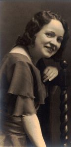 Photographie noir et blanc de Marie-Rose Descarries assise de côté sur une chaise en bois. Son bras gauche est appuyé sur le dossier.