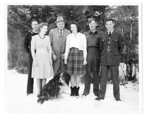 Six people, including 3 men in military uniform, outdoors in winter with dog