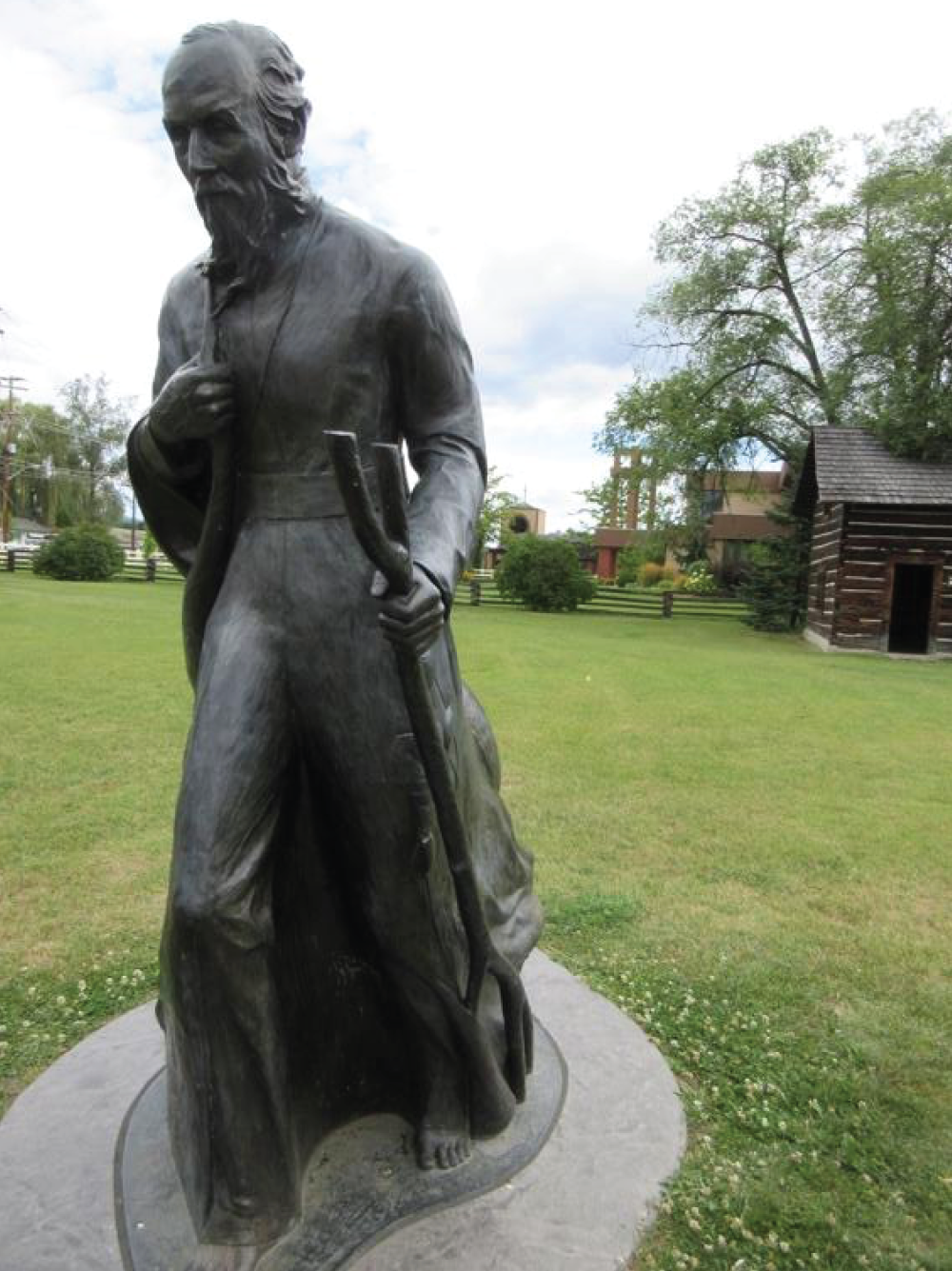 Statue d'un prêtre devant une cabane en rondins