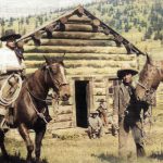 Deux cowboys avec leurs chevaux devant une cabane en rondins