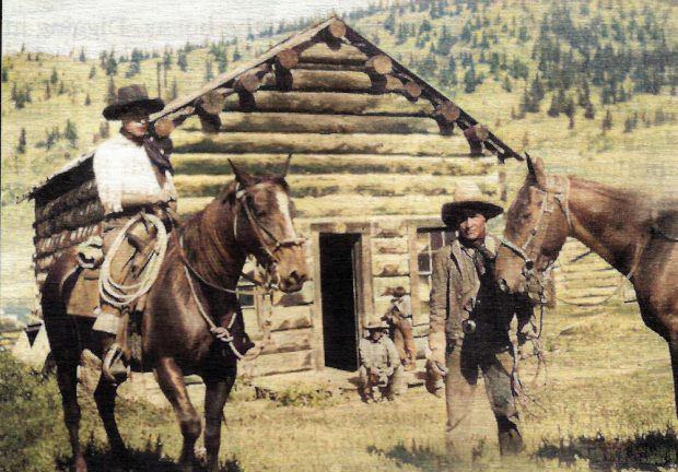 Deux cowboys avec leurs chevaux devant une cabane en rondins
