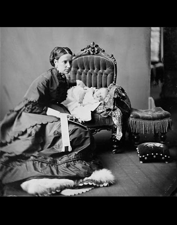 Photo noir et blanc de Lady Agnes Macdonald accroupie à côté d’une chaise sur laquelle repose son bébé, la petite Mary, en 1868. 