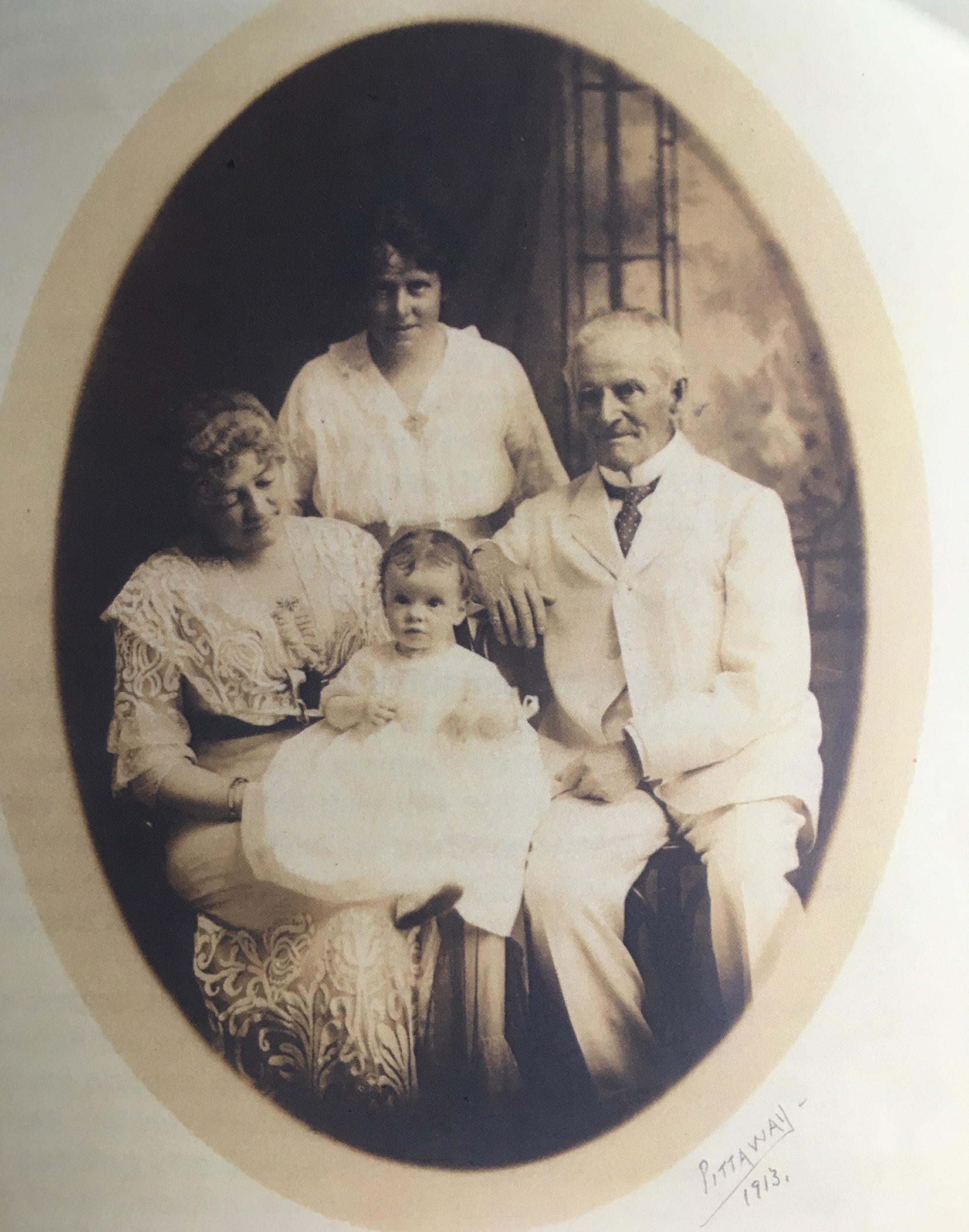 Photographie sépia ovale montrant quatre personnes (la famille Bate), dont un homme âgé (Sir Henry Bate), et deux femmes dont l’une (sa femme) est assise, un bébé (sa petite fille) sur ses genoux et l’autre (sa fille) se tenant debout derrière eux. Tous sont vêtus de blanc. 