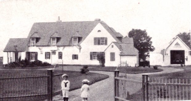 Photographie aux tons sépia d'une vaste maison (domaine de Kenneth Molson) entourée d'une clôture de fer avec portes; en avant-plan, on aperçoit deux jeunes enfants en costumes de matelots. 