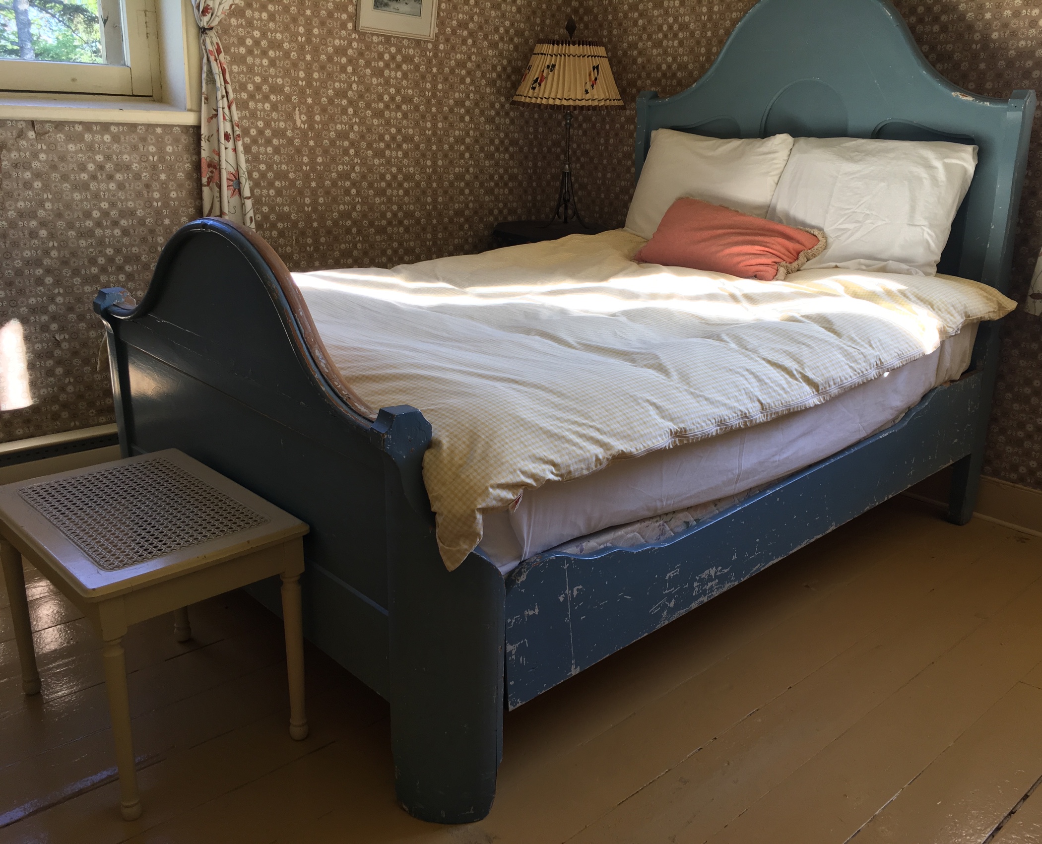 Photographie couleur d’un lit antique, le lit de Sir John A., en bois trois quarts, à tête haute et à pied plus bas, dont la peinture de couleur bleue est écaillée de façon marquée sur son côté. 