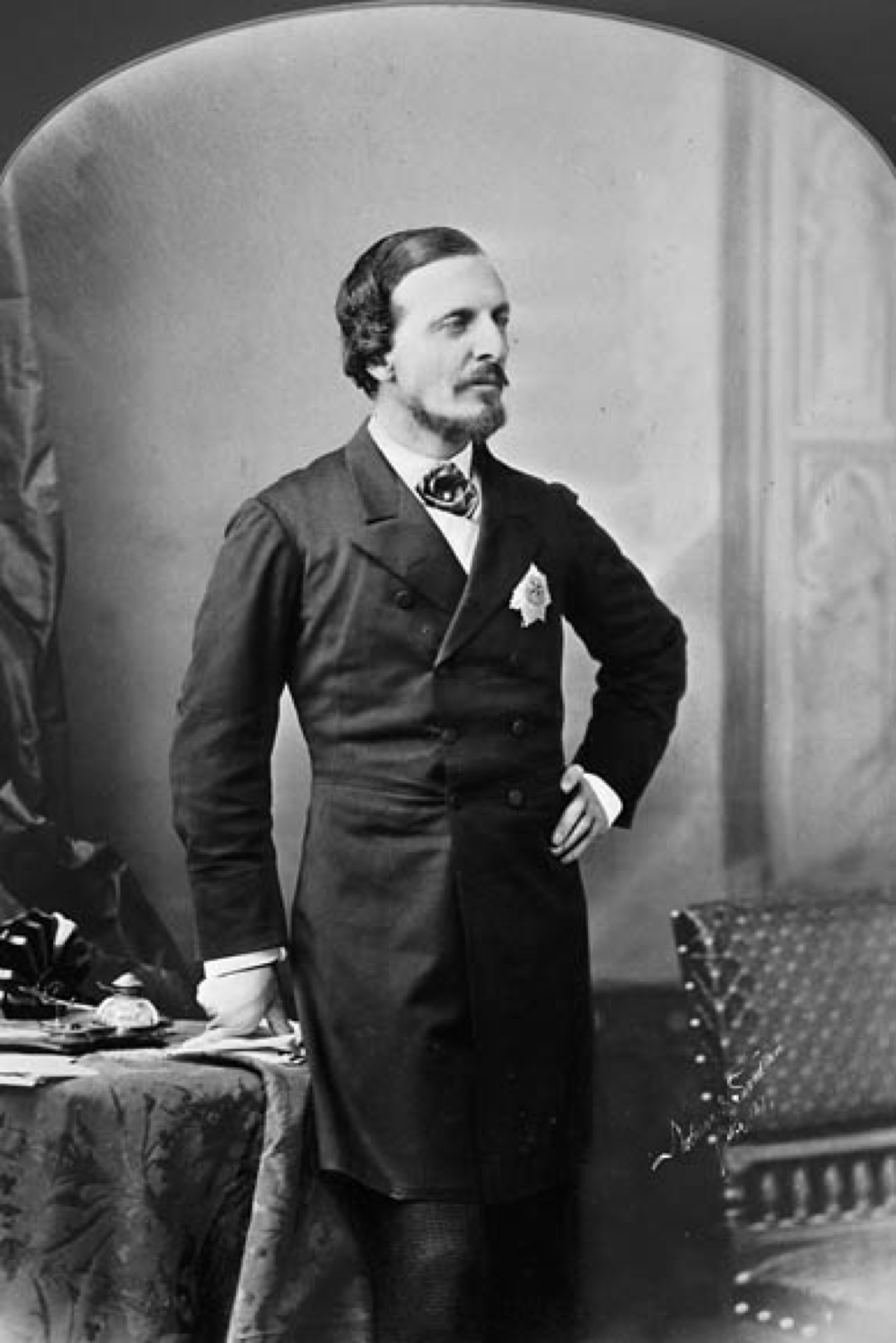 Portrait officiel en noir et blanc de Lord Dufferin posant dans un costume sombre à pochette frontale arborant un mouchoir blanc, sa main gauche posée sur sa hanche. 