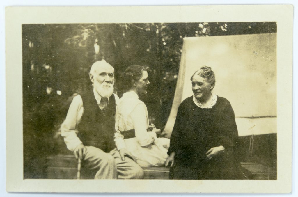Un homme barbu et deux femmes assis dehors, en tenue décontractée. 