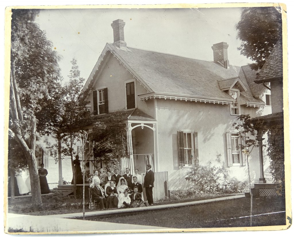 Image en noir et blanc d’un cortège nuptial assemblé à côté d’une maison