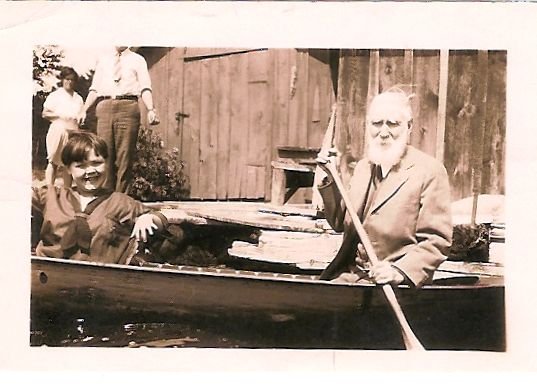 Des jeunes dans un canoë conduit par un homme âgé. Le quai et le hangar à bateaux sont visibles à l’arrière-plan.
