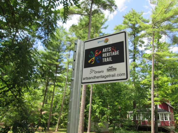 Enseigne en métal entourée d’arbres et un bâtiment dans le coin inférieur droit 