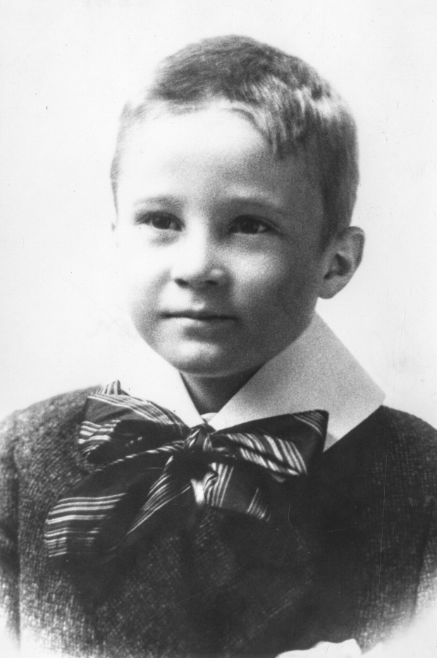 Photographie d’archive en noir et blanc d’un garçon vêtu d’un chandail, col blanc et nœud papillon attaché sous son menton.