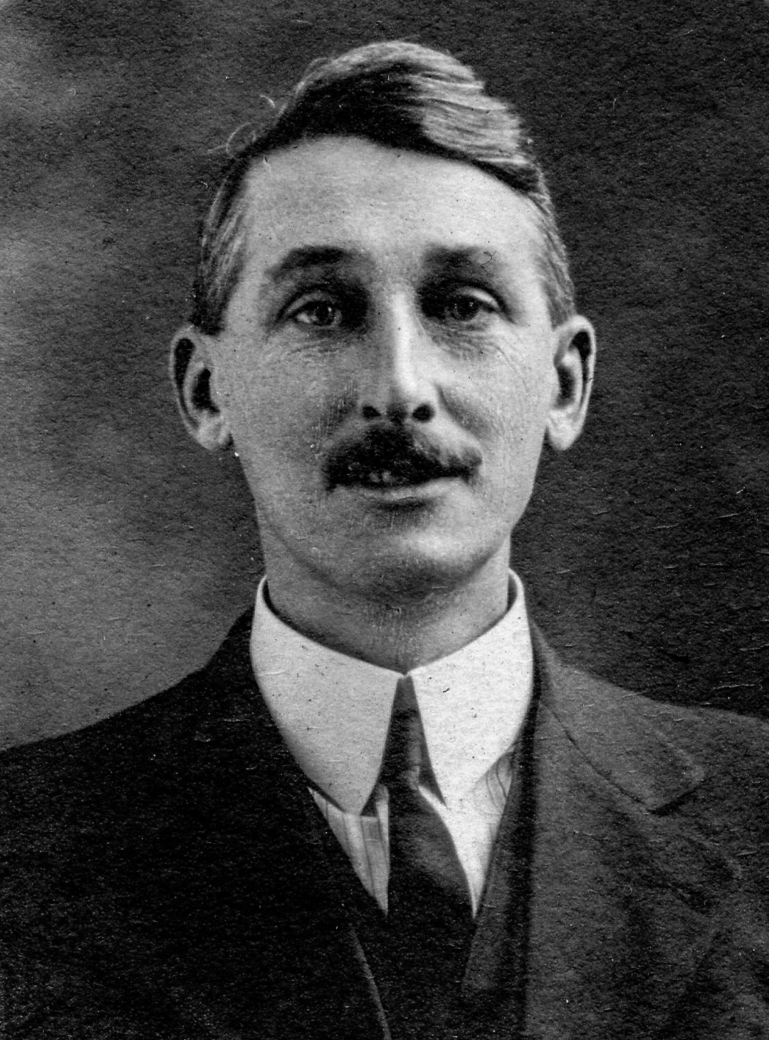 Photographie d’archive en noir et blanc d’un homme moustachu en costume-cravate.