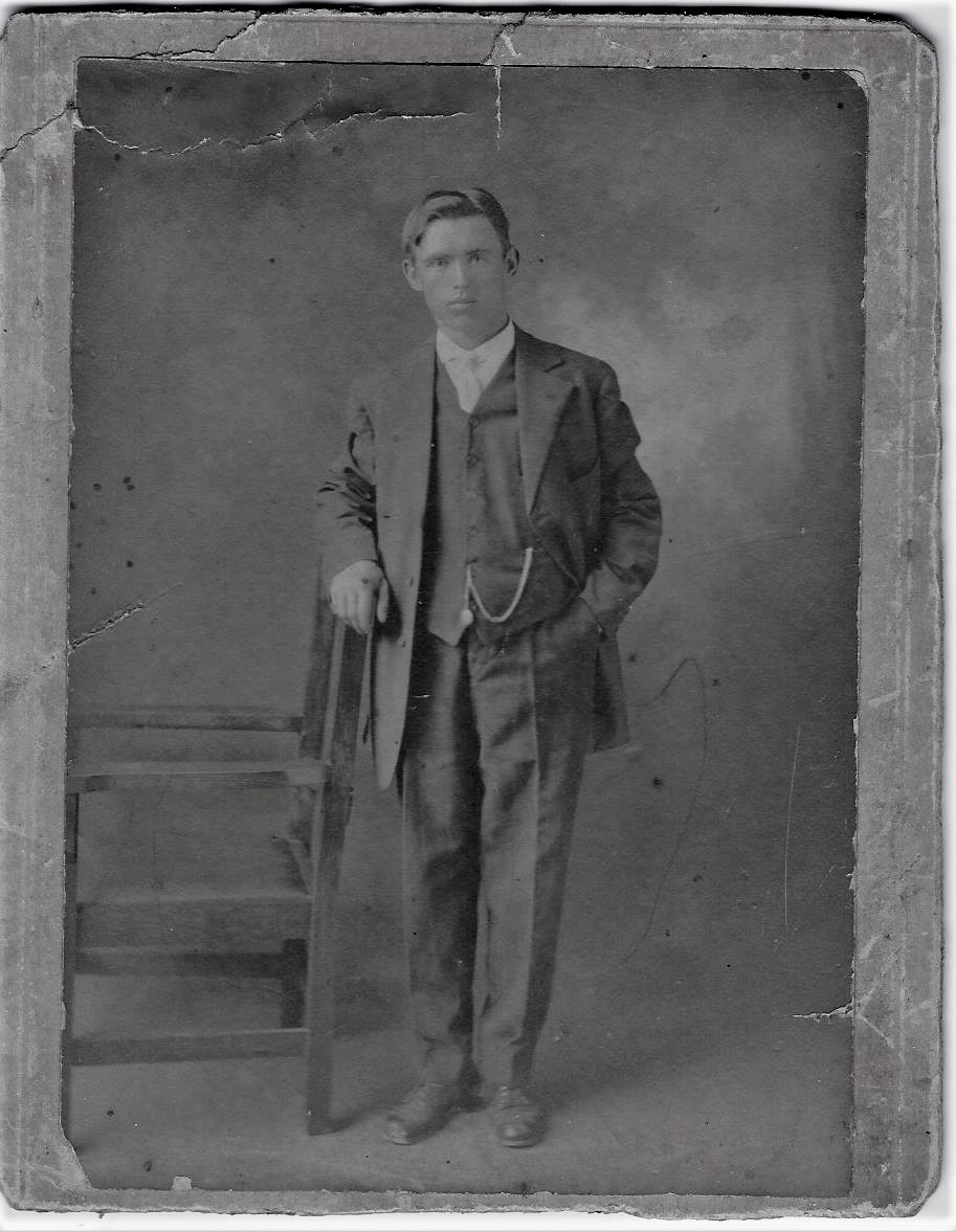 Photographie d’archive en noir et blanc d’un homme en costume-cravate s’appuyant sur une chaise.