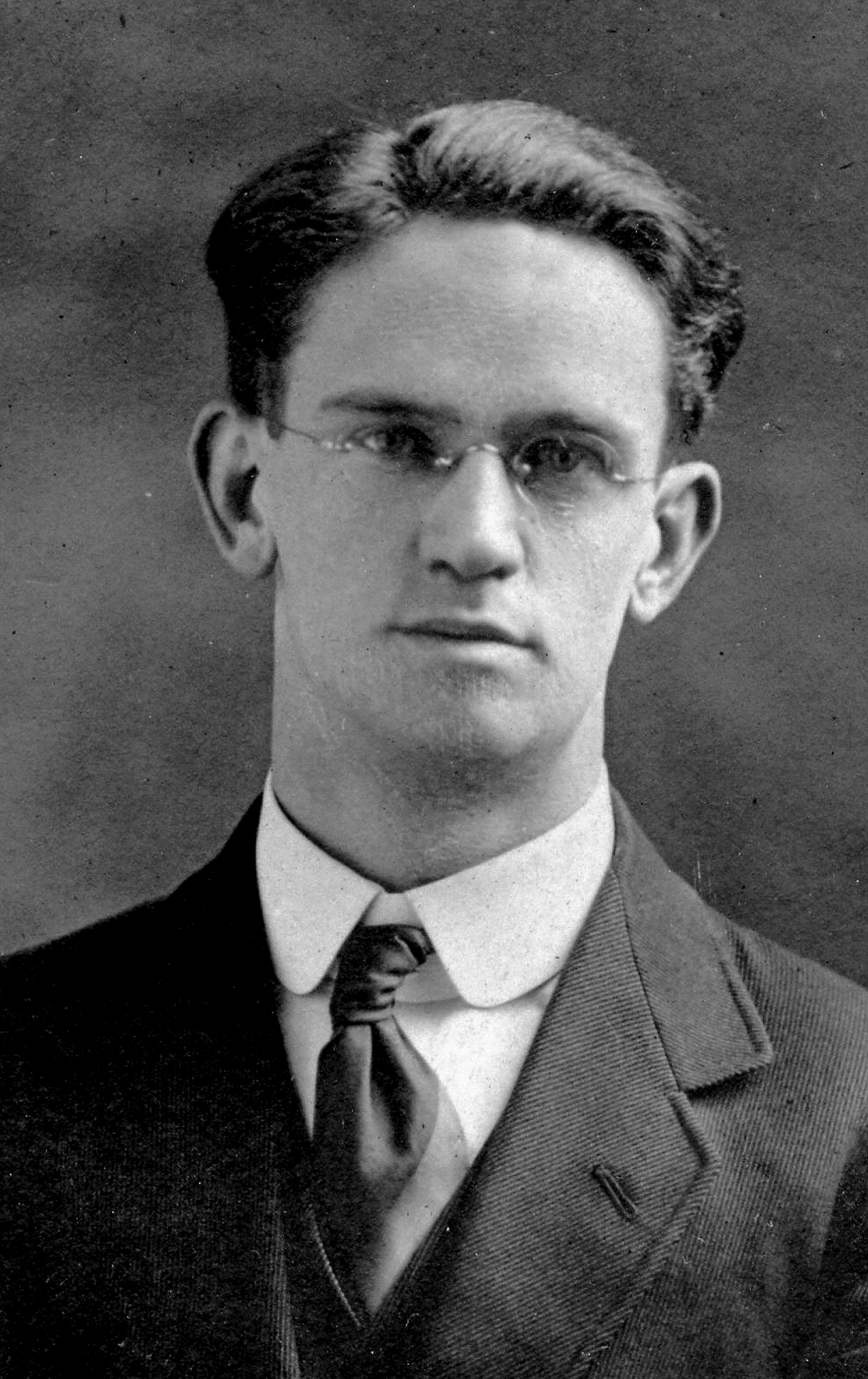 Photographie d’archive en noir et blanc d’un homme en costume-cravate portant des lunettes.