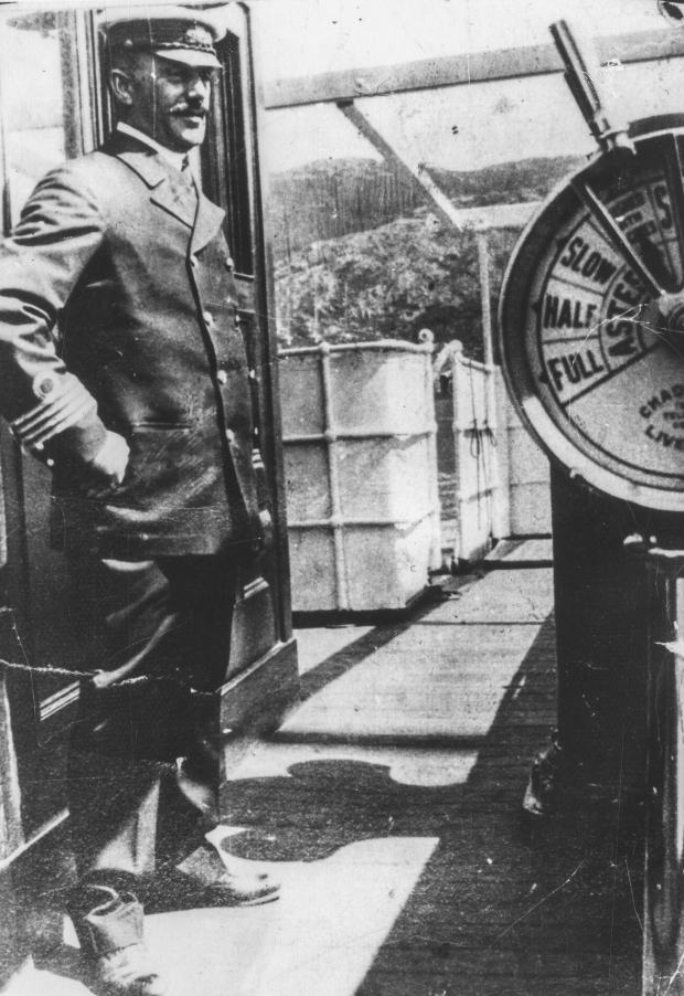Photographie d’archive en noir et blanc d’un homme en uniforme avec une casquette à visière se tenant debout sur le pont d’un bateau.