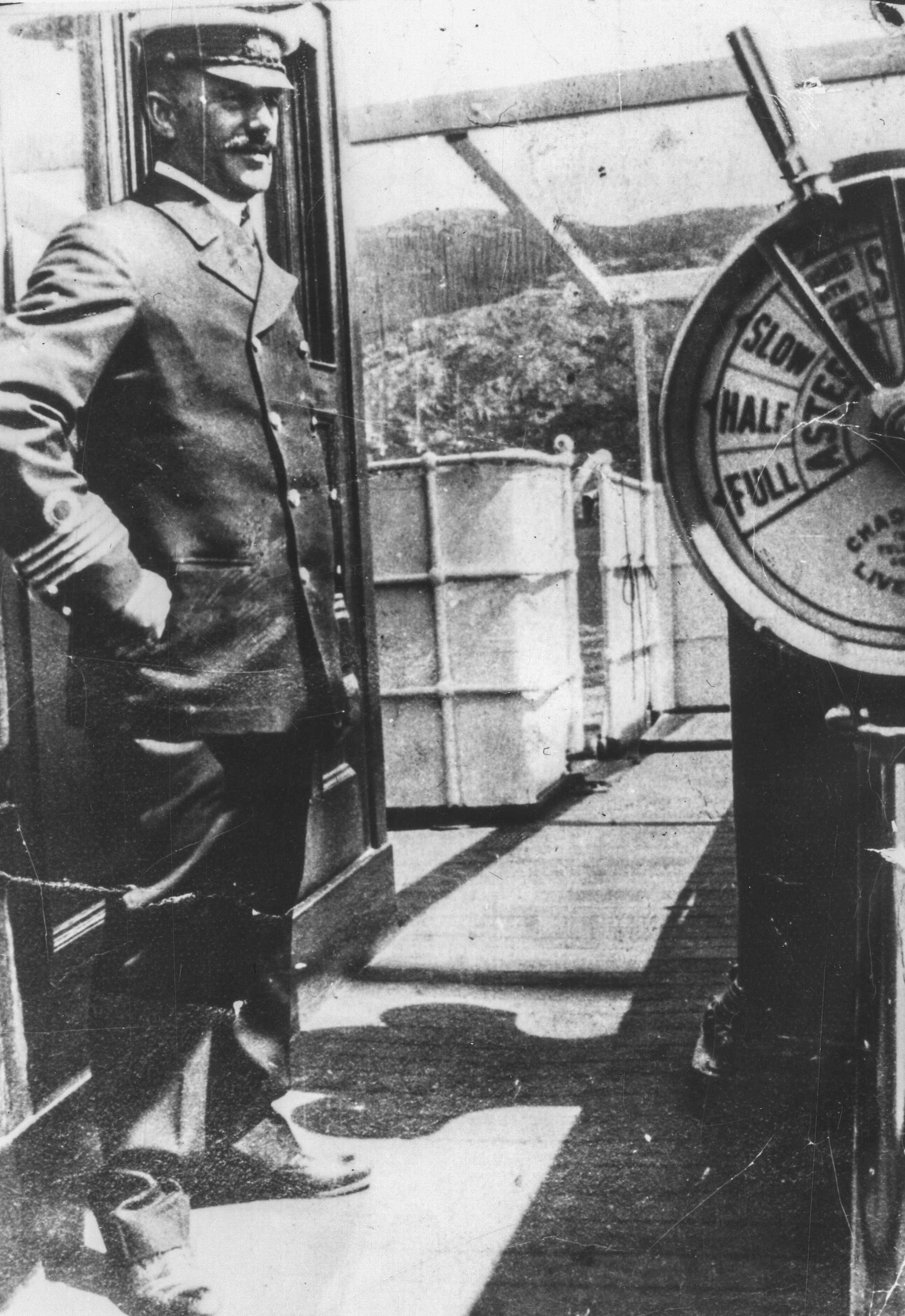 Photographie d’archive en noir et blanc d’un homme en uniforme avec une casquette à visière se tenant debout sur le pont d’un bateau.