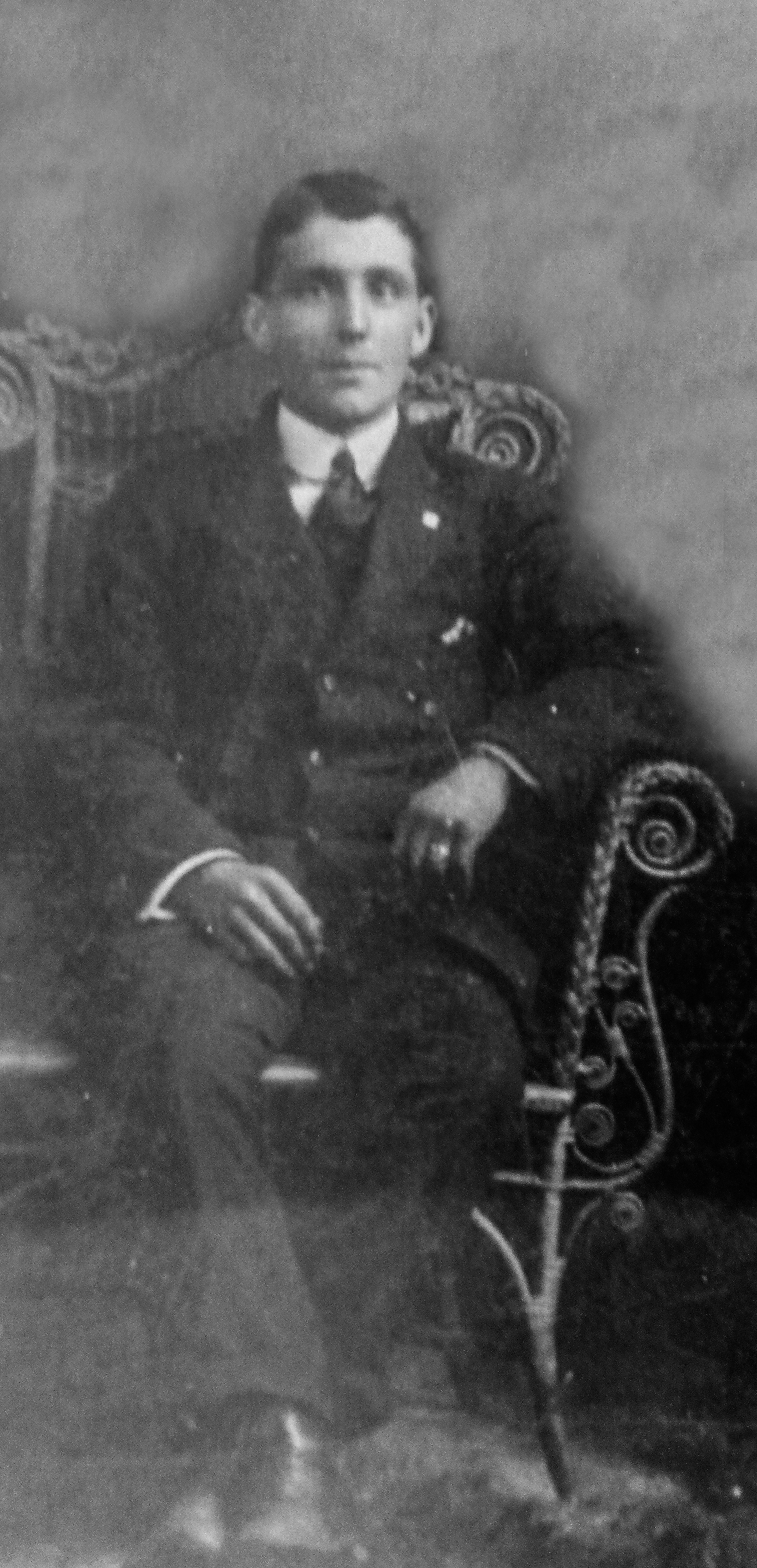 Photographie d’archive en noir et blanc d’un homme en costume-cravate assis dans un fauteuil.