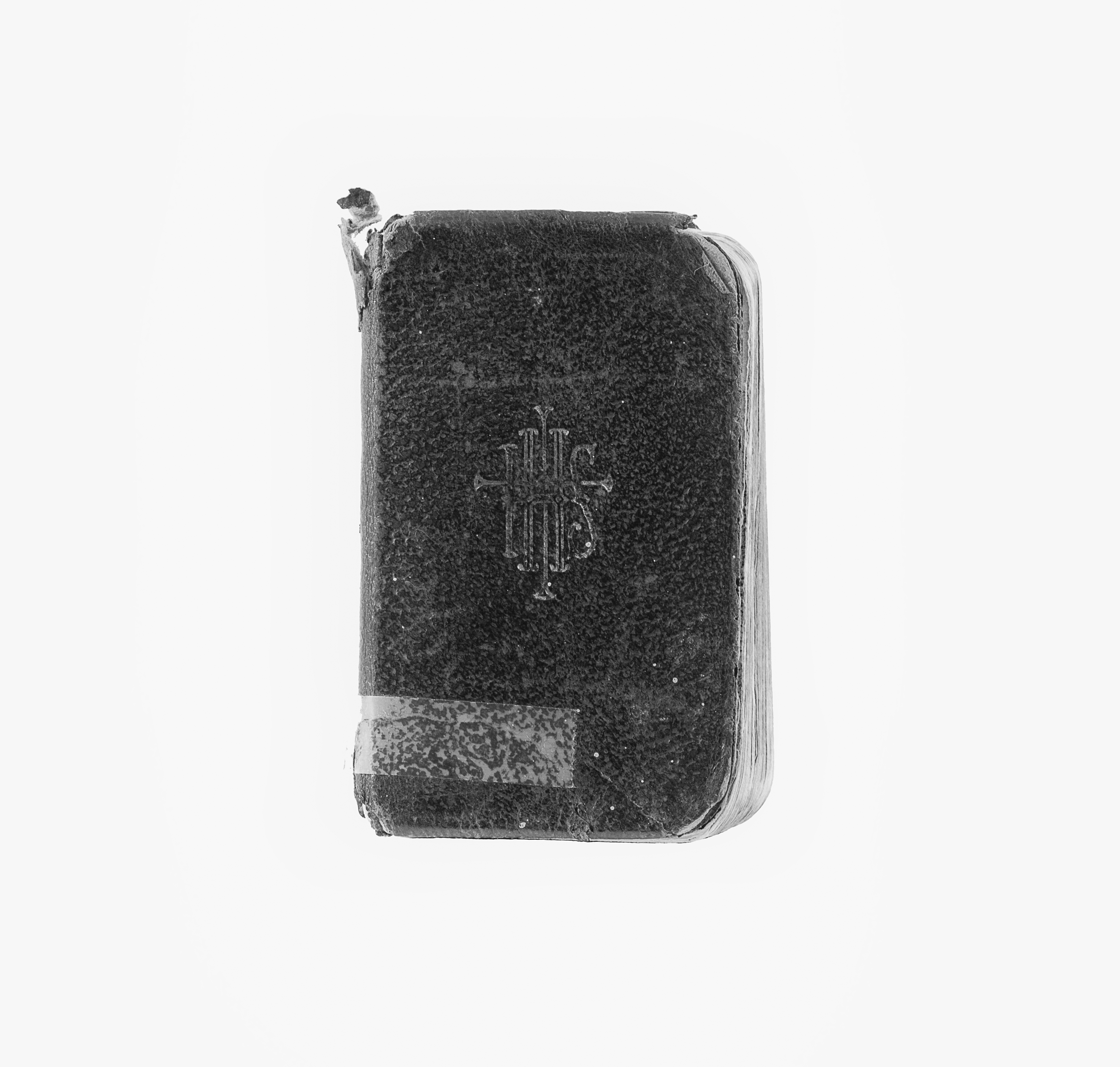 Photographie moderne en noir et blanc d’un livre de prières à la couverture noire et aux pages blanches. Sur la première de couverture est inscrit IHS.
