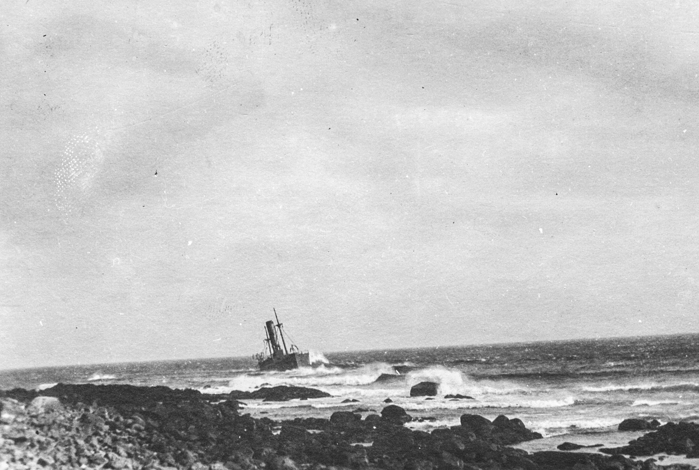 Photographie d’archive en noir et blanc d’un grand paquebot, le SS Florizel, échoué juste au large d’une plage rocheuse.