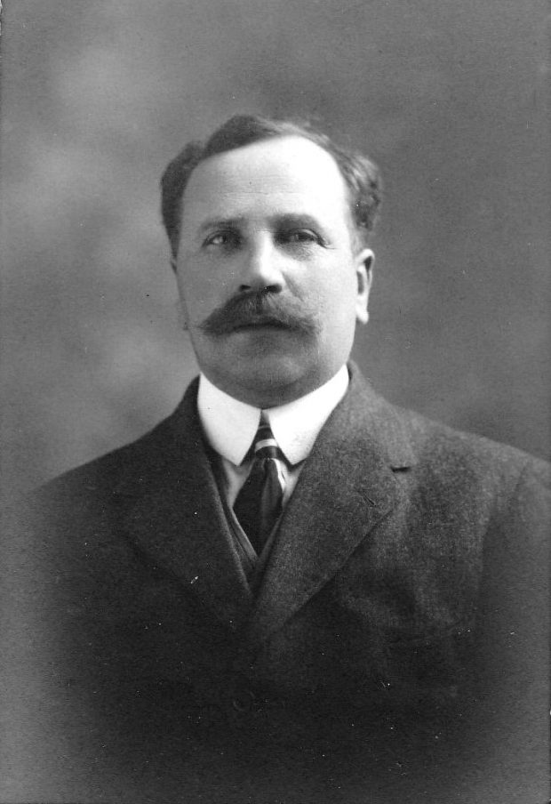 Photographie d’archive en noir et blanc d’un homme moustachu portant un costume-cravate.