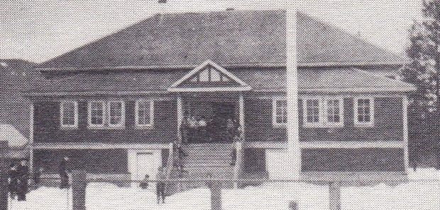 C’est l’hiver et des enfants sont rassemblés devant les marches d’une école. Plusieurs enfants jouent dans la neige dans la cour de l’école.