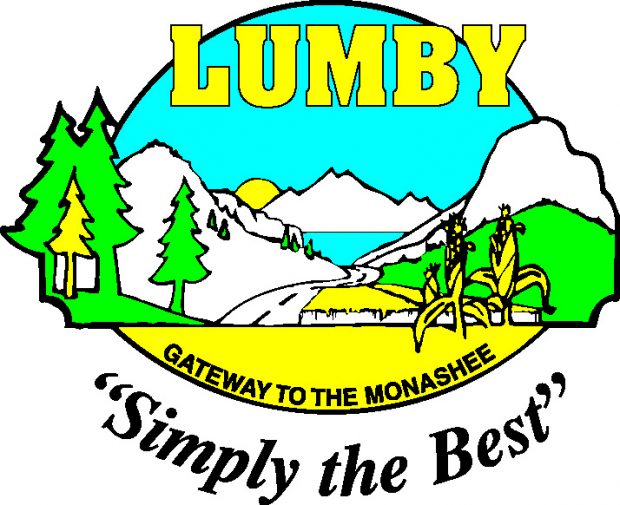 Un emblème a des montagnes et un lac. Au premier plan on voit des arbres et des tiges de maïs. Sur l’emblème c’est écrit : Lumby, la porte aux Monashees, simplement le meilleur.