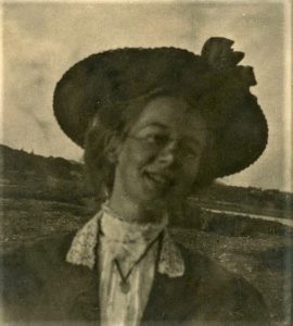 Portrait d’une jeune femme souriante portant un chemisier à col montant, un manteau à revers et un chapeau à rebord