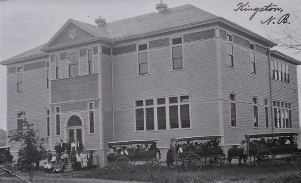 Enseignants et élèves posant sur les marches de l’école et dans trois fourgons scolaires. 