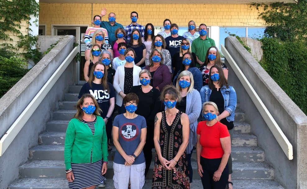 Groupe d’employés de l’école MCS sur les marches de l’établissement portant des masques de protection