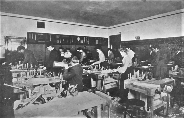 Étudiantes en jupe longue et étudiants en costume aux bancs de travail dans la salle de formation manuelle. 