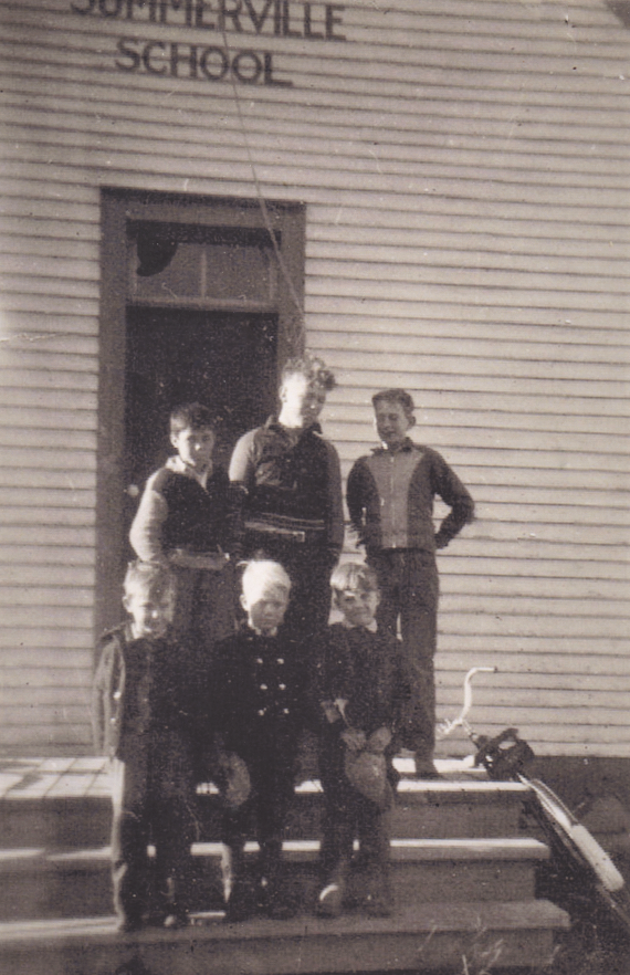 Six jeunes garçons posent dans les escaliers d’une école. Un vélo est appuyé contre le côté de l’escalier à droite.    