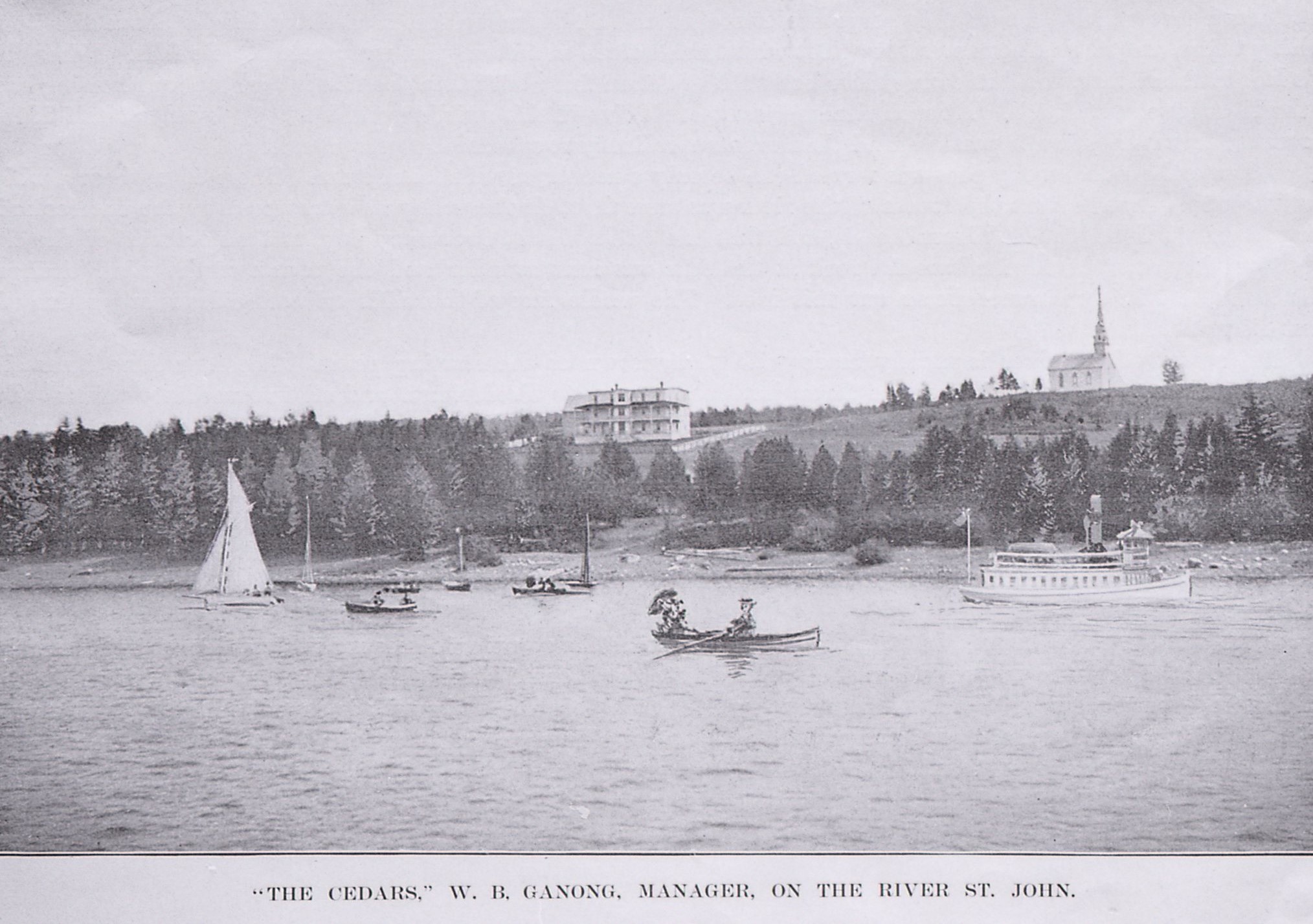 Vers 1900, un hôtel de trois étages près de la rive, sur la pente d’une colline surmontée d’une église avec une flèche en arrière-plan. Des personnes circulent dans des chaloupes, des voiliers et un bateau à vapeur au premier plan
