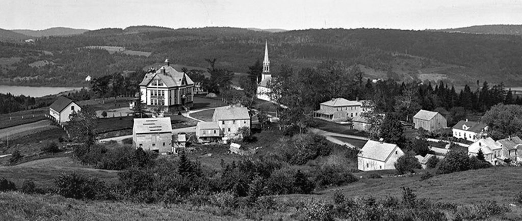 Vue aérienne de Kingston montrant les bâtiments historiques de l’école MCS, de l’église Trinity et du village au milieu de collines ondulantes, avec le lac Bates en arrière-plan à gauche et le ruisseau Kingston à droite..