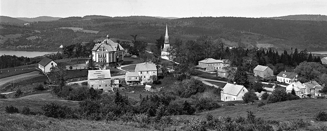 Vue aérienne de Kingston montrant les bâtiments historiques de l’école MCS, de l’église Trinity et du village au milieu de collines ondulantes, avec le lac Bates en arrière-plan à gauche et le ruisseau Kingston à droite..