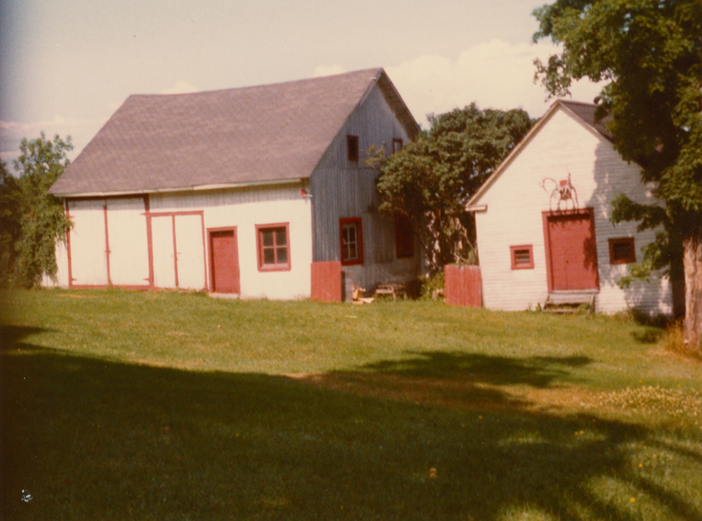 Photo couleur. Deux bâtiments dont les murs sont peints en blanc et les portes et fenêtres sont peintes en rouge.