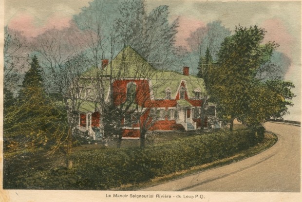 Image couleur. Maison de briques entourée d'une haie de cèdres et de nombreux arbres.