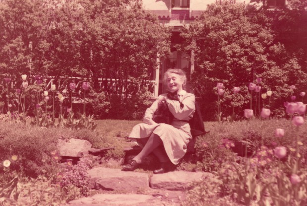 Photo couleur. Femme âgée assise au milieu de son jardin fleuri.