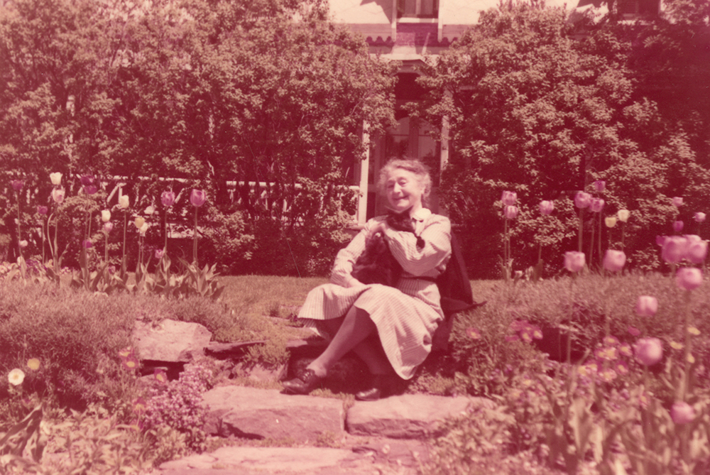 Photo couleur. Femme âgée assise au milieu de son jardin fleuri.