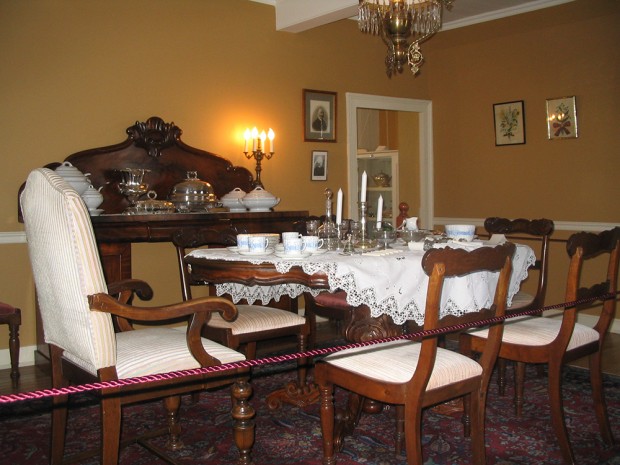 Photo couleur. À l’avant-plan, une table garnie et des chaises. Un imposant buffet en bois à l’arrière-plan.