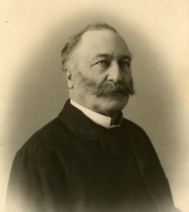 Photo noir et blanc. Portrait d'un homme moustachu aux cheveux grisonnants portant un veston noir.