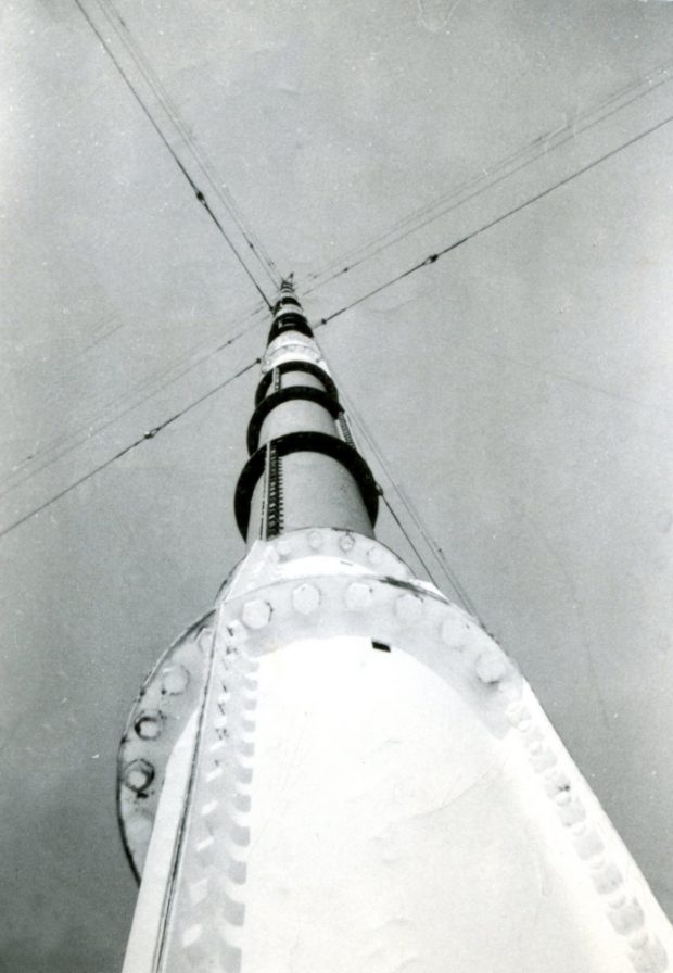 Pylône radio, vue depuis sa base jusqu’à son sommet. Une série de câbles de soutien s’étendent vers l’extérieur dans quatre directions.