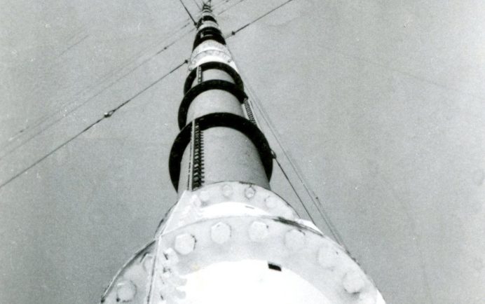 Pylône radio, vue depuis sa base jusqu’à son sommet. Une série de câbles de soutien s’étendent vers l’extérieur dans quatre directions.