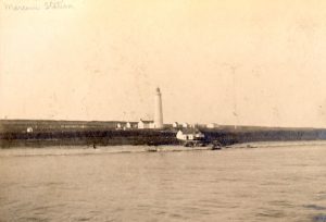 Phare et quelques petits bâtiments sur un littoral peu élevé.