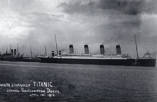 Un grand navire à quatre cheminées quitte un port par la droite, laissant derrière lui des navires plus petits. La photographie porte l'inscription suivante : « Paquebot de la White Star Line 'Titanic'. Quittant les quais de Southampton, le 10 avril 1912. » (Traduction)